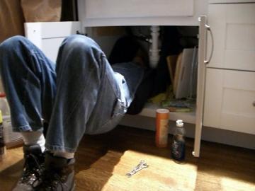 Plumbing technician under sink works on drain pipes 